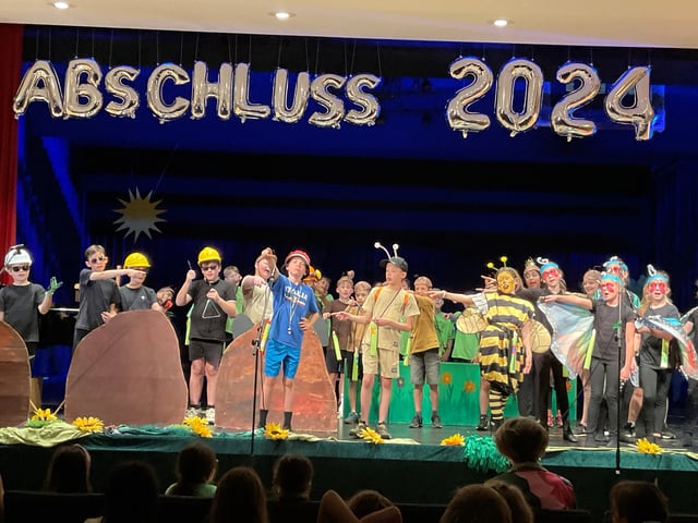 Verkleidete Kinder, darunter Bienen und Schmetterlinge, stehen bei der Abschlussfeier 2024 auf der Bühne.