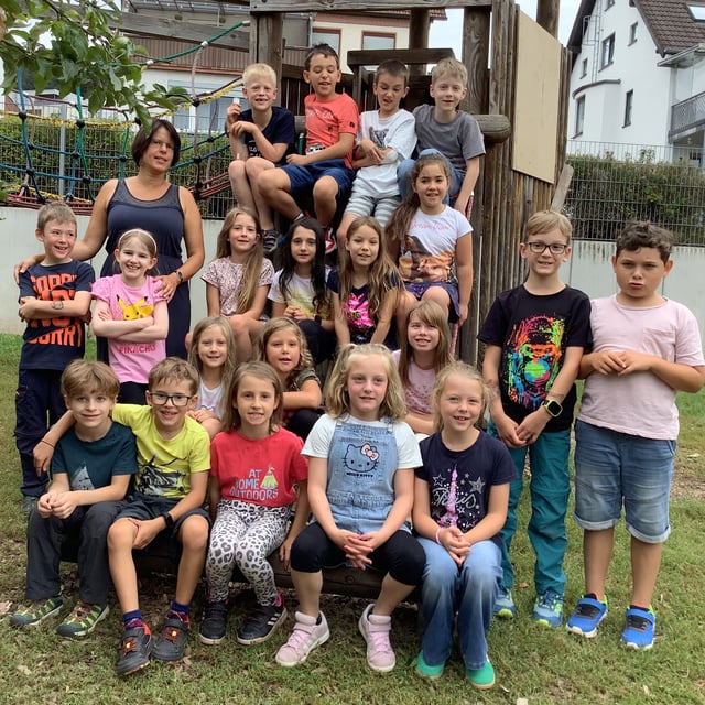 Eine Schulklasse posiert mit ihrer Lehrkraft für ein Gruppenfoto am Klettergerüst auf dem Schulhof.